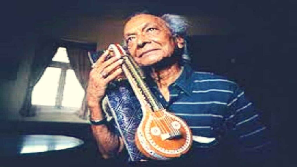 Elderly Indian musician holding traditional string instrument inside a room