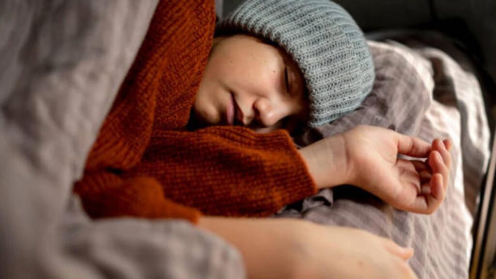 A person sleeping in winter while wearing a sweater under a blanket