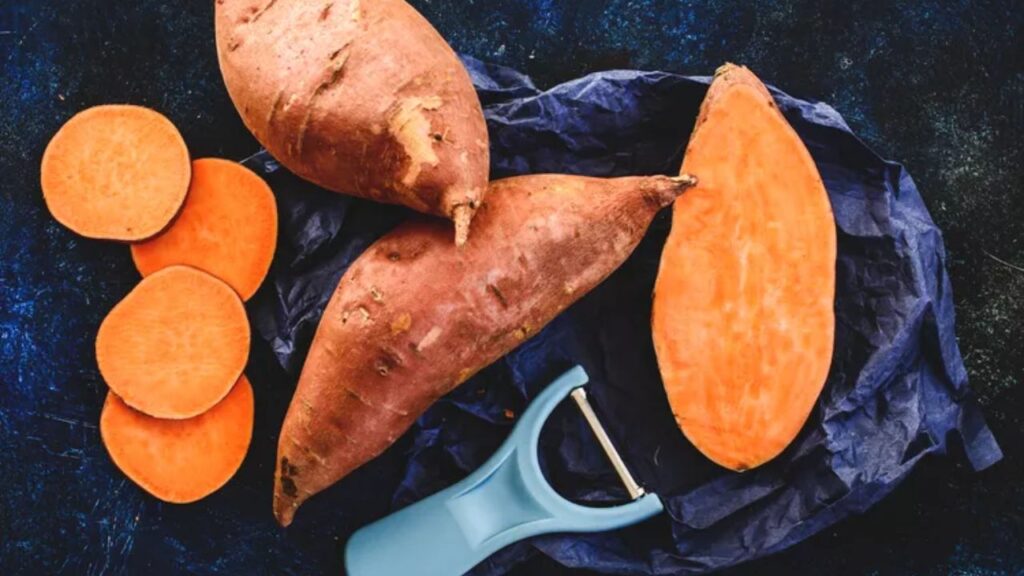 Sweet potatoes whole and sliced on a dark surface, illustrating a healthy carbohydrate food option.