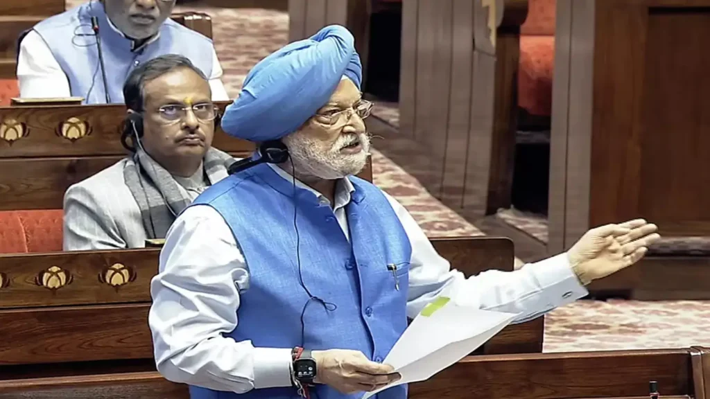 Union Minister Hardeep Singh Puri speaking in Parliament, wearing a blue turban and vest, holding papers.