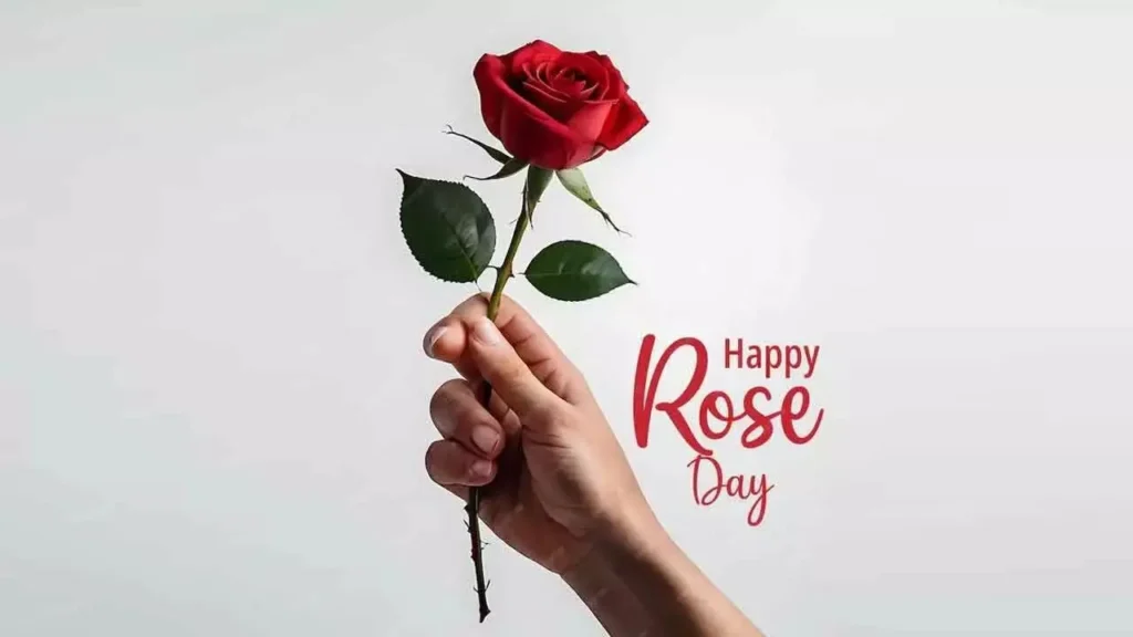 A hand holding a single red rose against a white background for Rose Day 2026.