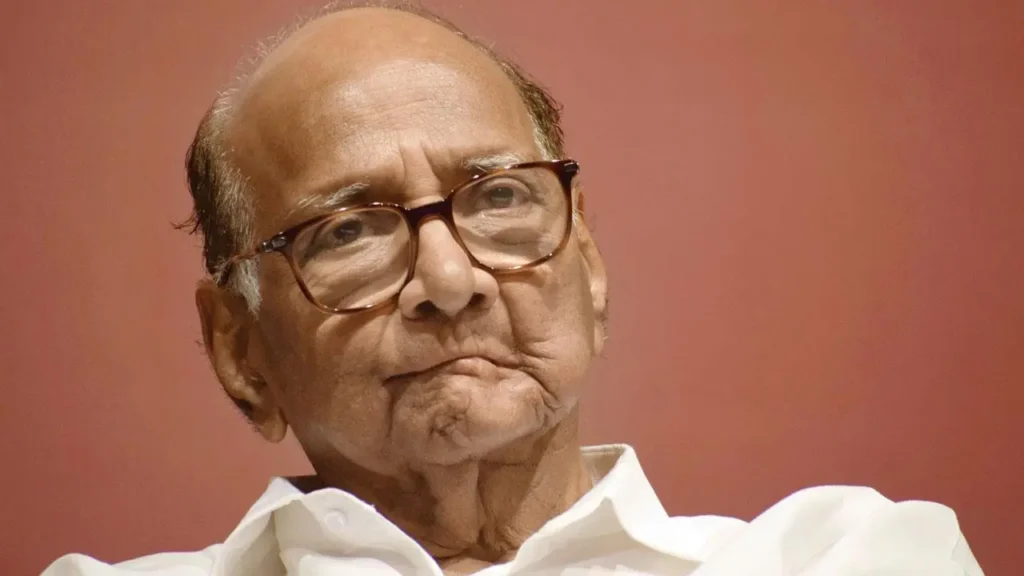 NCP leader Sharad Pawar speaking at a public event in a white shirt and glasses.
