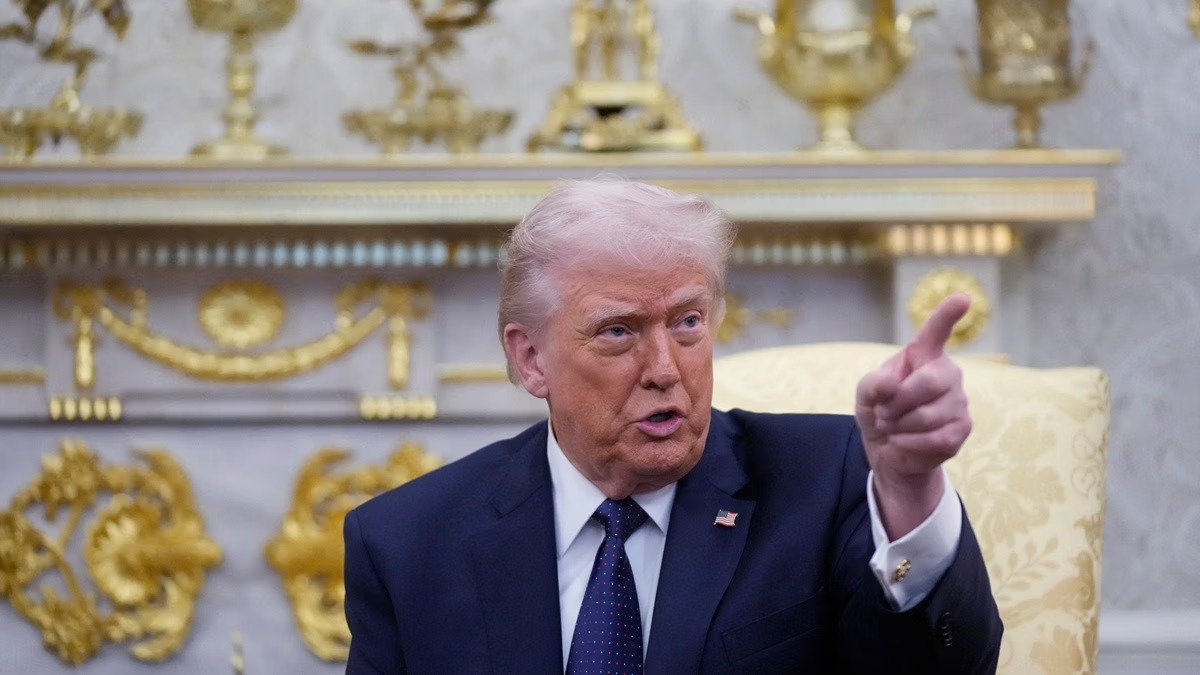 US President Donald Trump speaking, with an oil tanker in the Strait of Hormuz in the background.